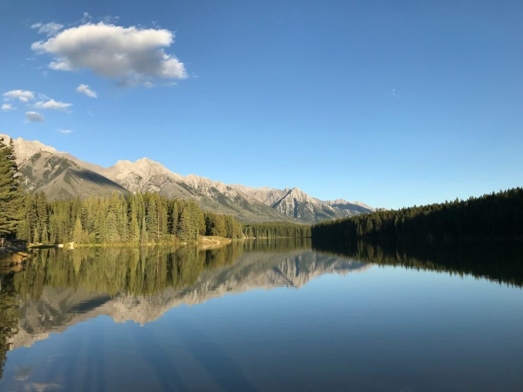 lake near green trees and mountain under blue sky during daytime